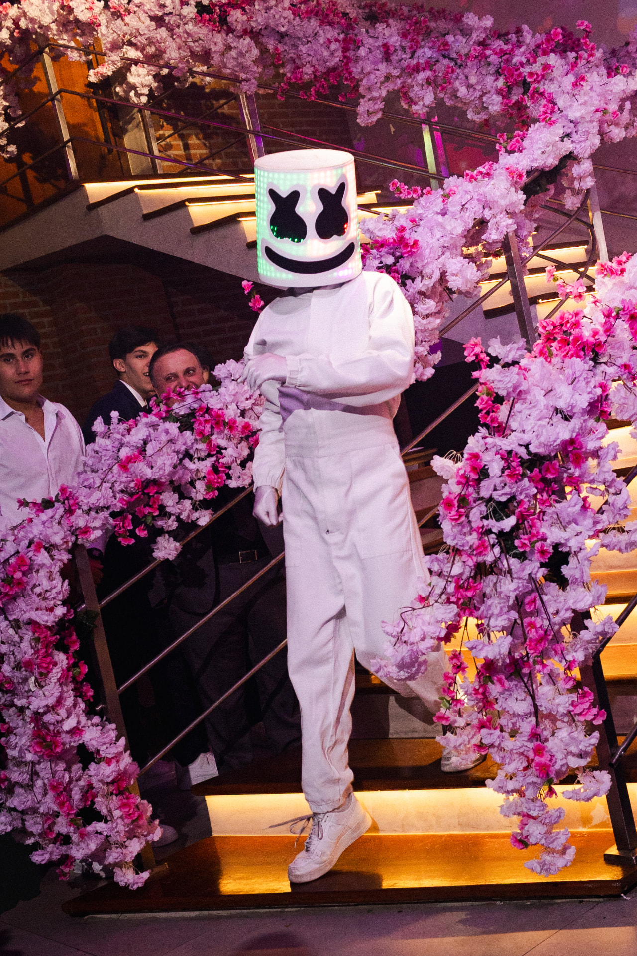 Performer com máscara de LED descendo escada florida de cerejeiras durante festa de 15 anos
